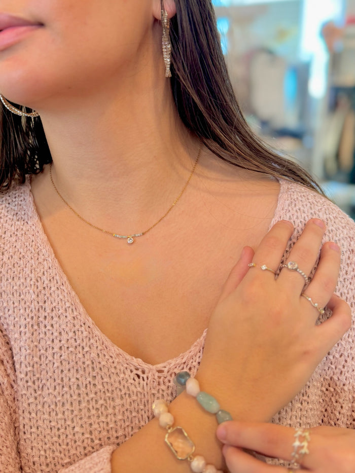 Close-up of a person wearing jewelry including earrings, necklace, rings, and bracelets.