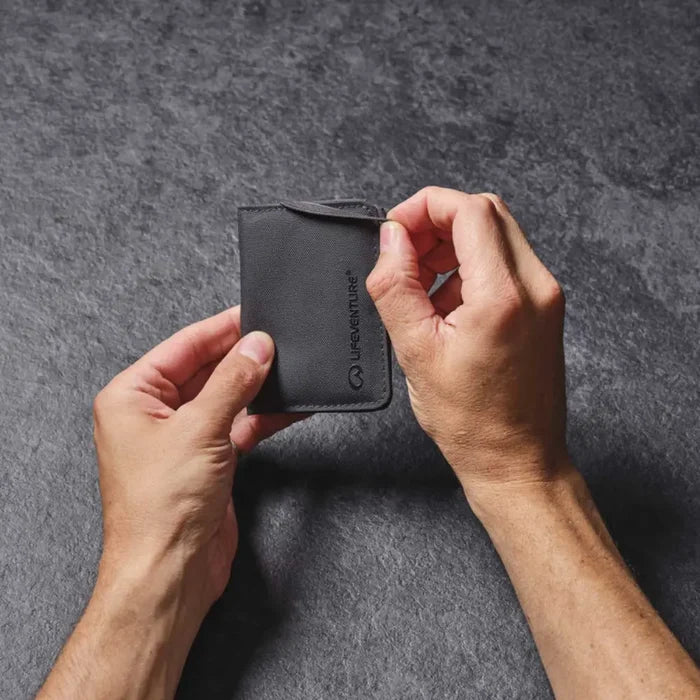 Person holding a closed Lifeventure RFID card wallet with one hand removing the elasticated closure strap on a grey background