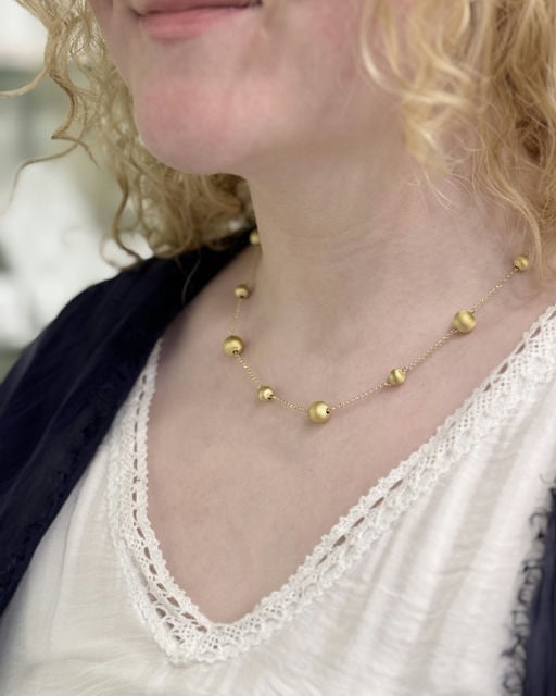 Model wearing a gold plated sterling silver necklace with brushed bead stations, styled with a lace-trim top and dark cardigan