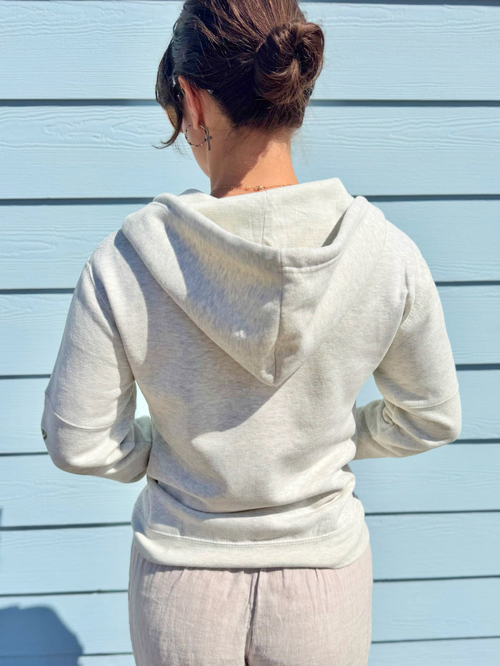 Person wearing a light gray hoodie and pants against a light blue wall.