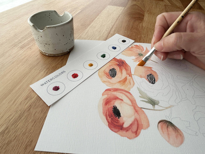 Person painting flowers with watercolors on a wooden table