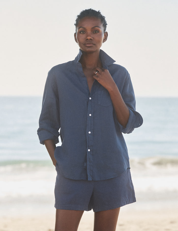Woman wearing a blue shirt and shorts standing on a beach.