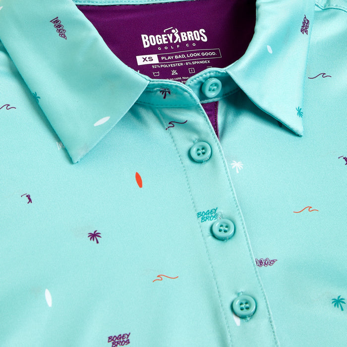 Close-up of the Beach - Women's Polo: a turquoise shirt with playful prints, athletic fit, collar, four-button placket, purple inner collar, and XS size tag for style and comfort.