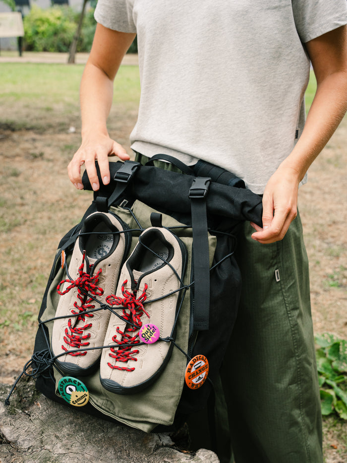 Bridge Backpack in Black outdoors with shoes secured under the front bungee cord