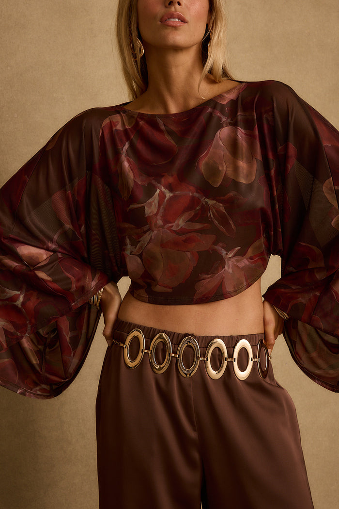 Close-up of sheer mulberry floral mesh crop top with billowing sleeves and gold ring belt.