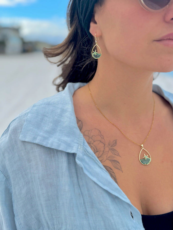 Person wearing a gold necklace with a blue pendant outdoors