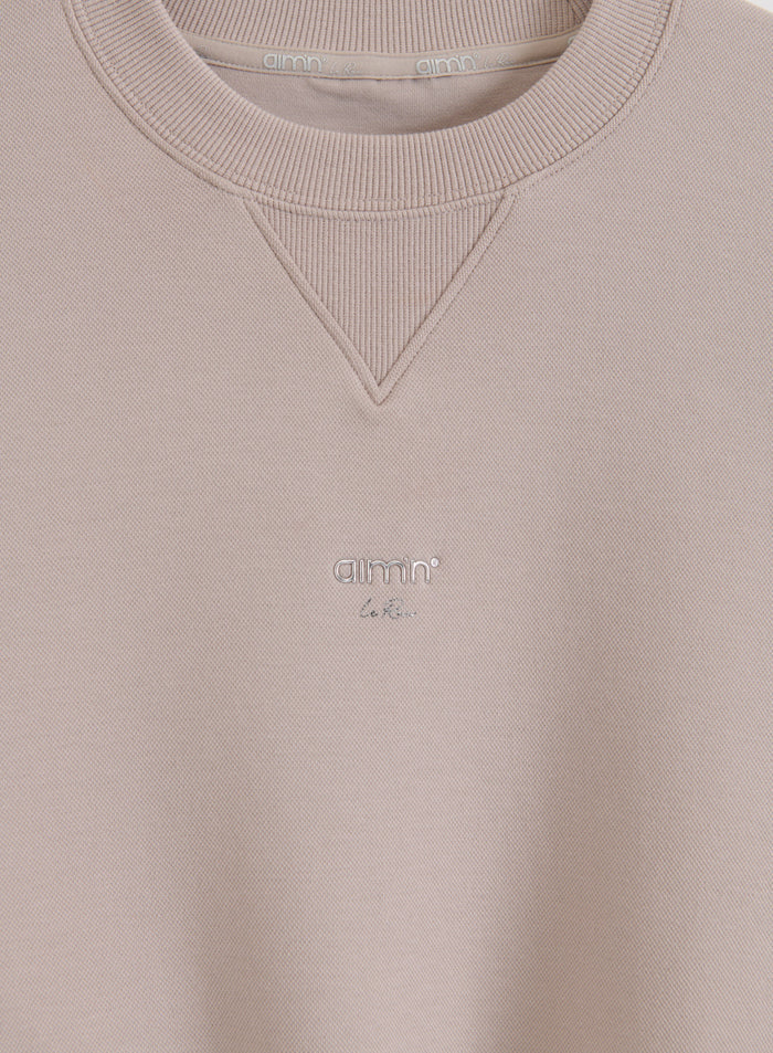 Logoyksityiskohta ja joustinneulottu pääntie Dark Clay aim'n Le Run Running Sweatshirt -paidassa.