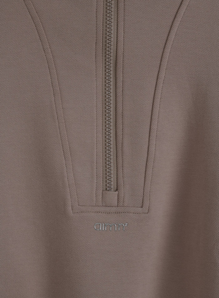 Dark Clay Sportif Half Zip Hood, jossa on ryhdikäs jersey-kangas, puolivetoketju ja metallinen aim'n-logo.