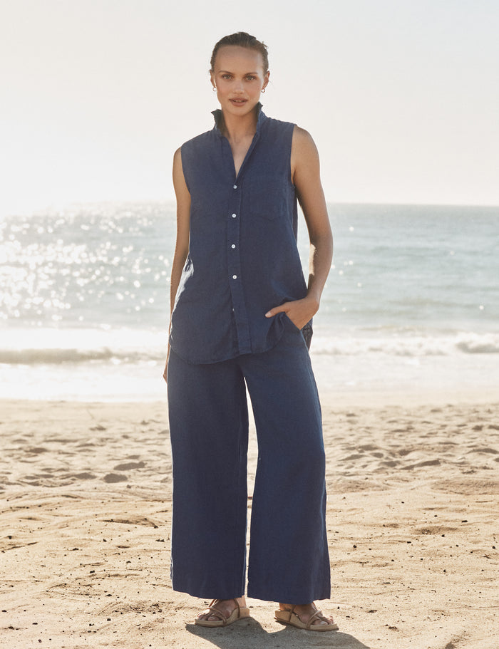 Woman in navy sleeveless top and wide-leg pants standing on a beach.