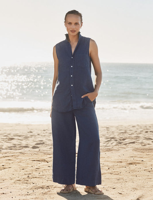Woman in navy sleeveless top and wide-leg pants standing on a beach.