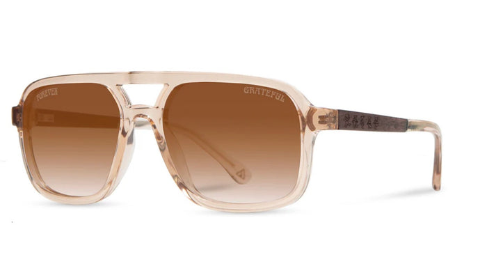 Angled view of Camp Eyewear Grateful Dead Forever sunglasses featuring a translucent champagne frame, walnut wood temples, and warm brown gradient polarized lenses.