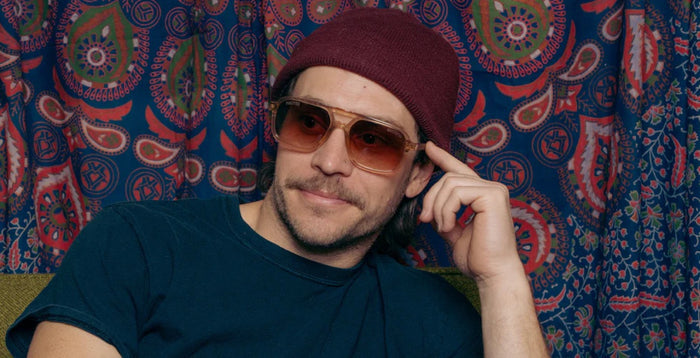 Person wearing Camp Eyewear Grateful Dead Forever sunglasses with a translucent champagne frame, walnut wood temples, and brown gradient polarized lenses.