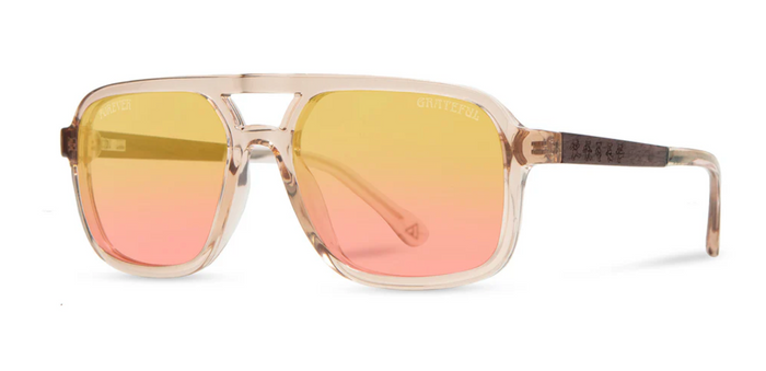 Angled view of Camp Eyewear Grateful Dead Forever sunglasses featuring a translucent champagne frame, walnut wood temples, and warm yellow-to-pink gradient polarized lenses.