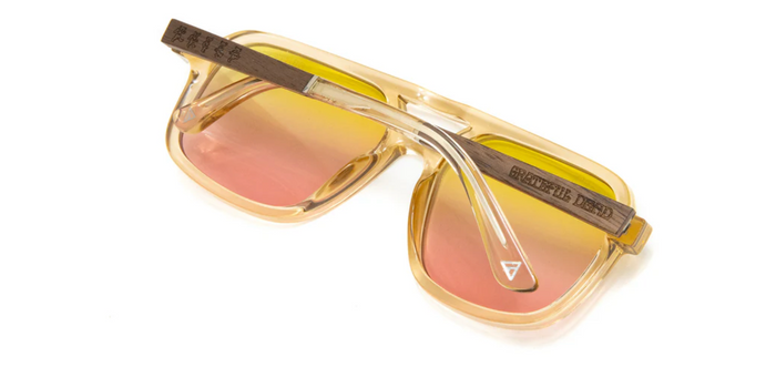 Back view of Camp Eyewear Grateful Dead Forever sunglasses showing engraved walnut wood temples, translucent champagne frame, and yellow-to-pink gradient lenses.