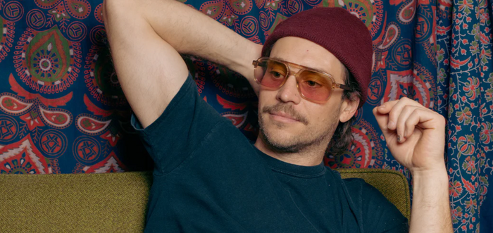 Person wearing Camp Eyewear Grateful Dead Forever sunglasses with translucent champagne frames, walnut wood temples, and warm gradient yellow-to-pink lenses.