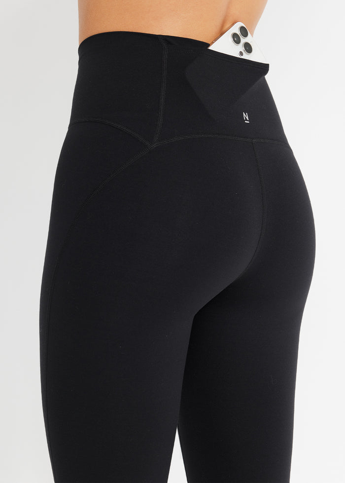 Close-up of hidden waistband pocket on black leggings with phone tucked inside