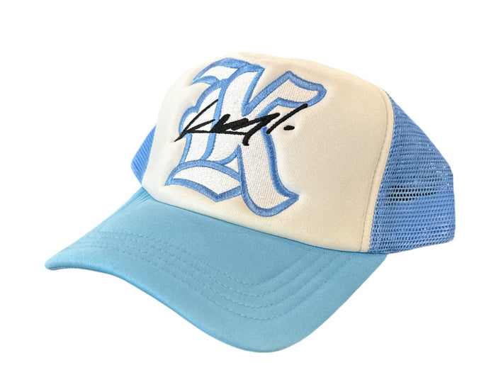 White and Carolina blue KML ‘K’ trucker hat by KAAMIL with mesh back and curved brim, casual outdoor headwear.
