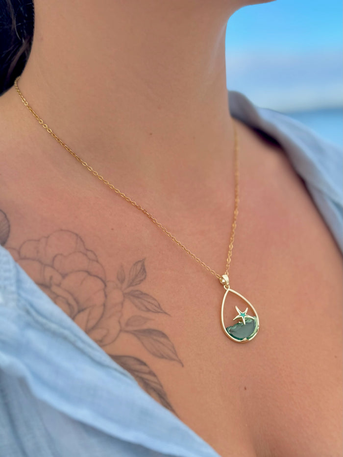 Gold necklace with a blue pendant worn by a person against a blurred background