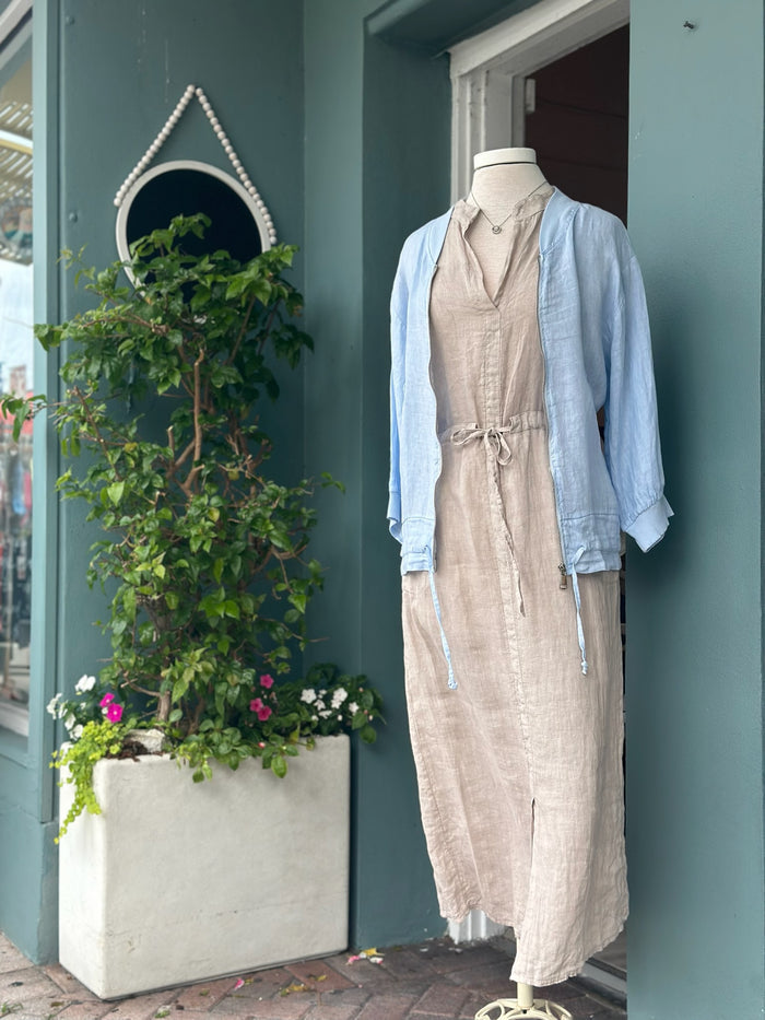 Light blue linen zip-front jacket with ribbed collar and cuffs, styled over a neutral linen dress. Features a relaxed fit, lightweight fabric, side pockets, and adjustable drawstring hem details.