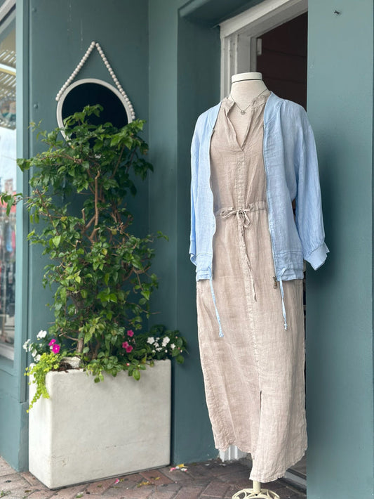 Light blue linen zip-front jacket with ribbed collar and cuffs, styled over a neutral linen dress. Features a relaxed fit, lightweight fabric, side pockets, and adjustable drawstring hem details.