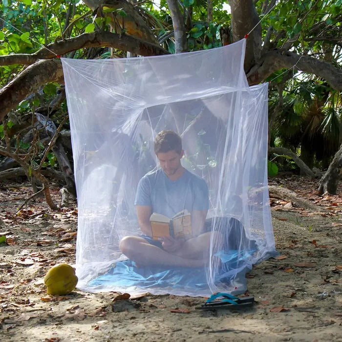 A man reading a book inside a set-up Lifesystems Boxnet single mosquito net in a mangrove