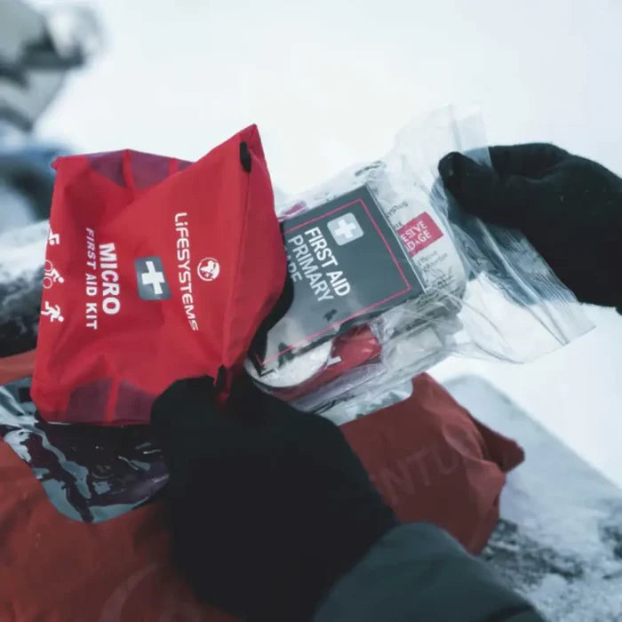 A person removing items from a Lifesystems Light And Dry Micro First Aid Kit in the snow