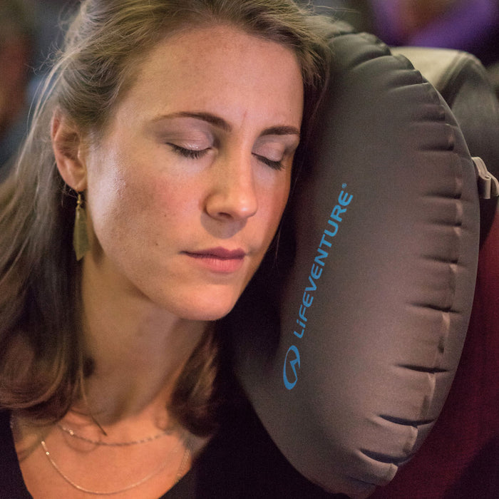 Woman using a Lifeventure inflatable travel pillow as a neck rest on a flight