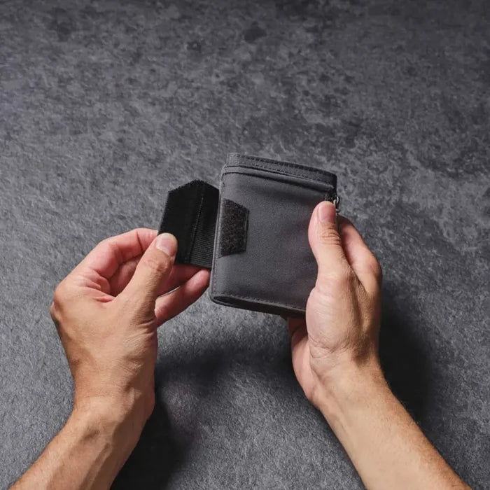 Person holding a Lifeventure RFiD Tri-Fold Wallet with the left hand opening the loop and hoop closure system, on a grey background