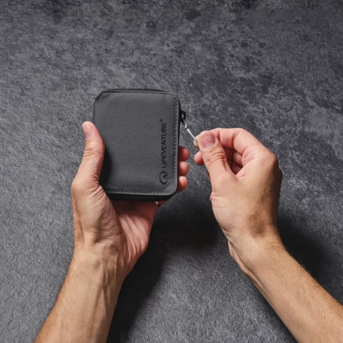 Personpulling the zip on a Lifeventure RFiD Zipped Bi-Fold Wallet, on a grey background