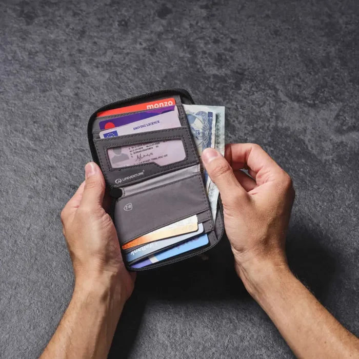 Person holding open a  Lifeventure RFiD Zipped Bi-Fold Wallet showing cards and bank notes, on a grey background