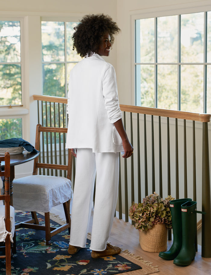 Person wearing a white outfit standing in a room with large windows and green boots.