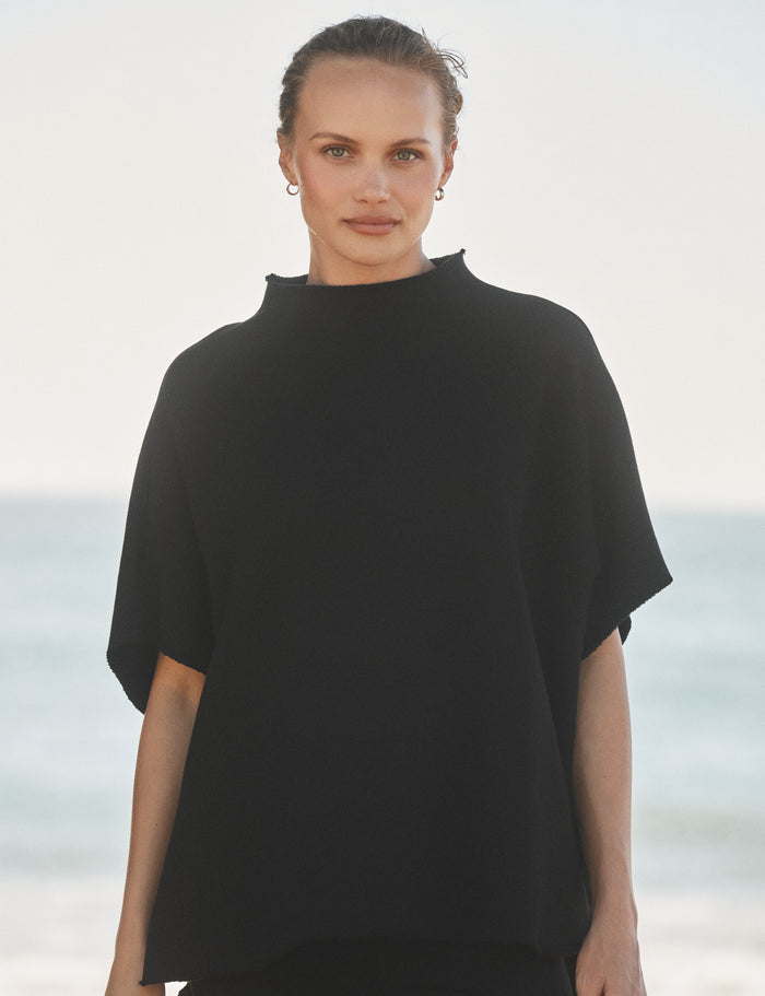 Woman wearing a black capelet with a blurred beach background