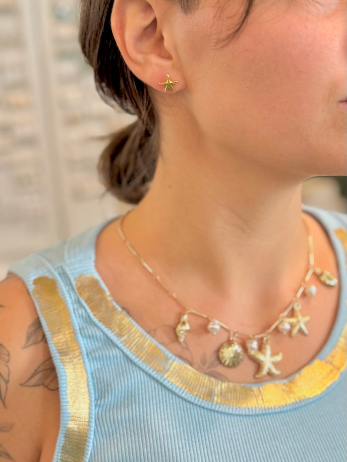 Close-up of a person wearing a necklace with starfish and shell charms, with a blurred background.