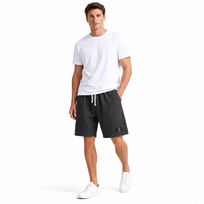 Closer view of men's linen shorts showing the solid color fabric, relaxed outline, and embroidered black label accent detail.