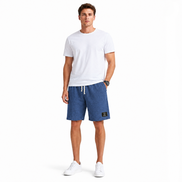 Men's linen beach shorts displayed with a loose fit profile, simple solid color look, and embroidered black label detail now.