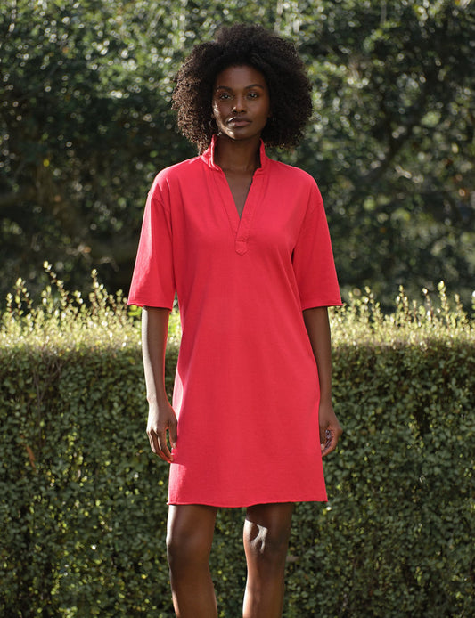 Woman wearing a red dress standing outdoors with greenery in the background