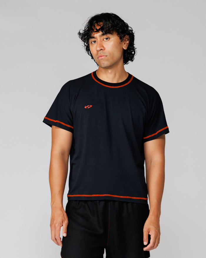 Model wearing Outnback Bog Tee in black, straight-on front view showing orange trim stitching