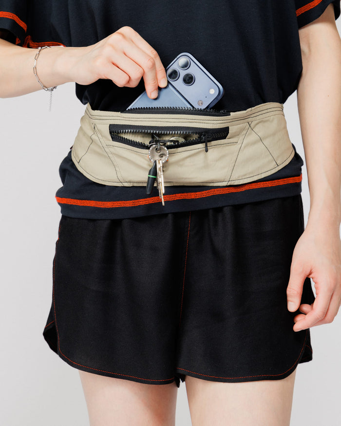 Close view of a phone and keys being stowed in the Outnback Running Strap in stone worn at the waist