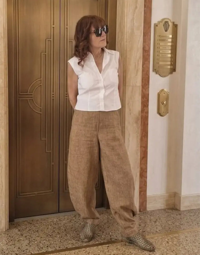 Person wearing a white sleeveless top and beige pants standing in front of a door.