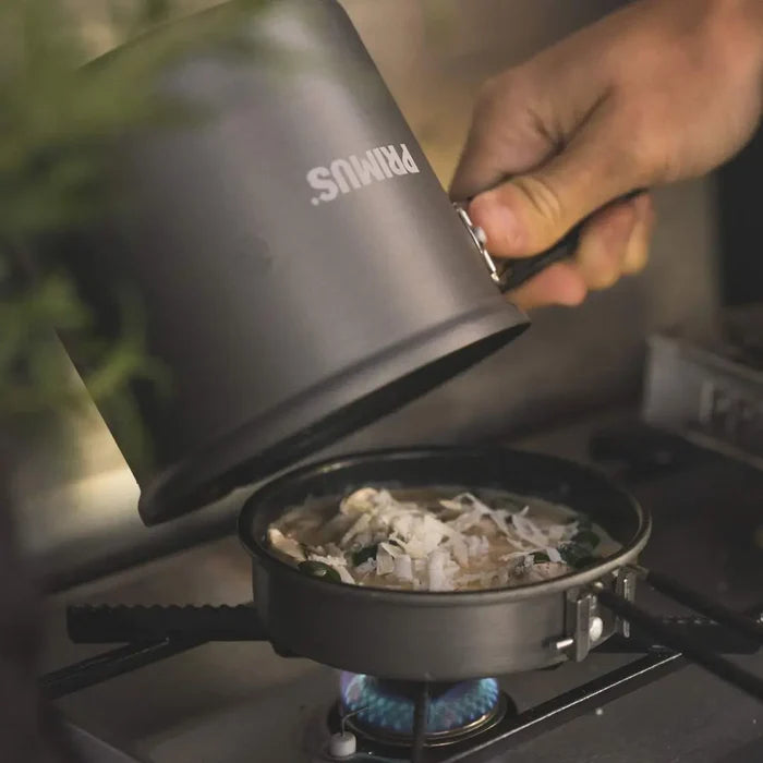 Person emptyingthe contents of their Primus Litech trek kettle into the frying pan lid on a camping stove