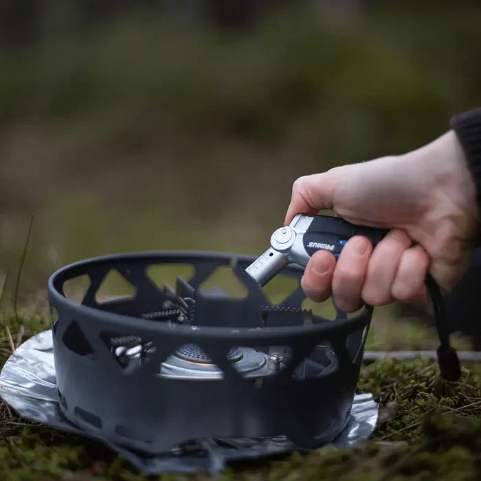 Person igniting a camping stove with a black Primus Power lighter in a natural setting