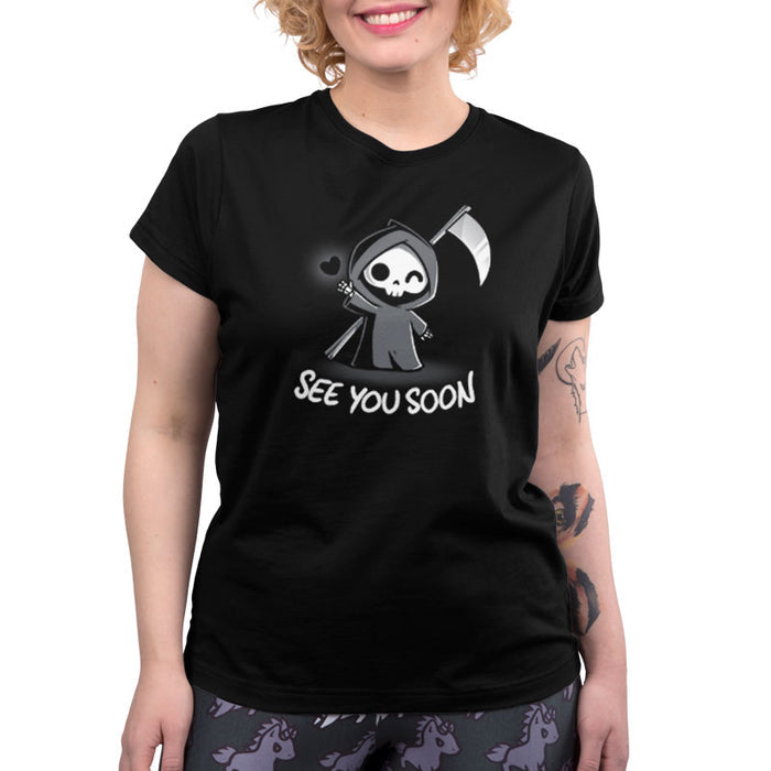 Premium Cotton T-shirt_TeeTurtle See You Soon black t-shirt featuring a spooky cartoon Grim Reaper holding a scythe, waving, and a floating black heart next to it, with the text below that says in dark humor "SEE YOU SOON".