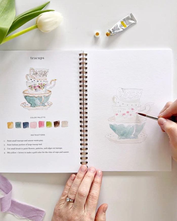 Open Spring watercolor workbook by Emily Lex showing teacups watercolor lesson with step by step instructions and outlined sketch on thick paper