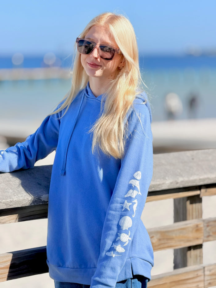Woman wearing a periwinkle blue hoodie with a beach background