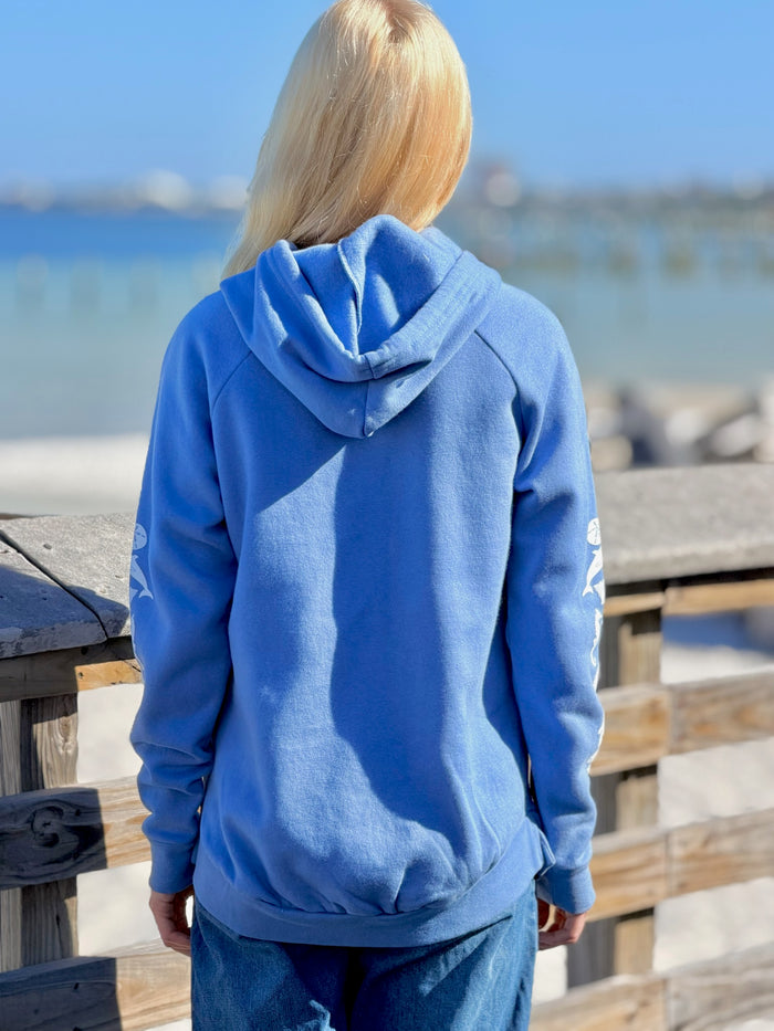 Person wearing a blue hoodie standing on a wooden deck by the water