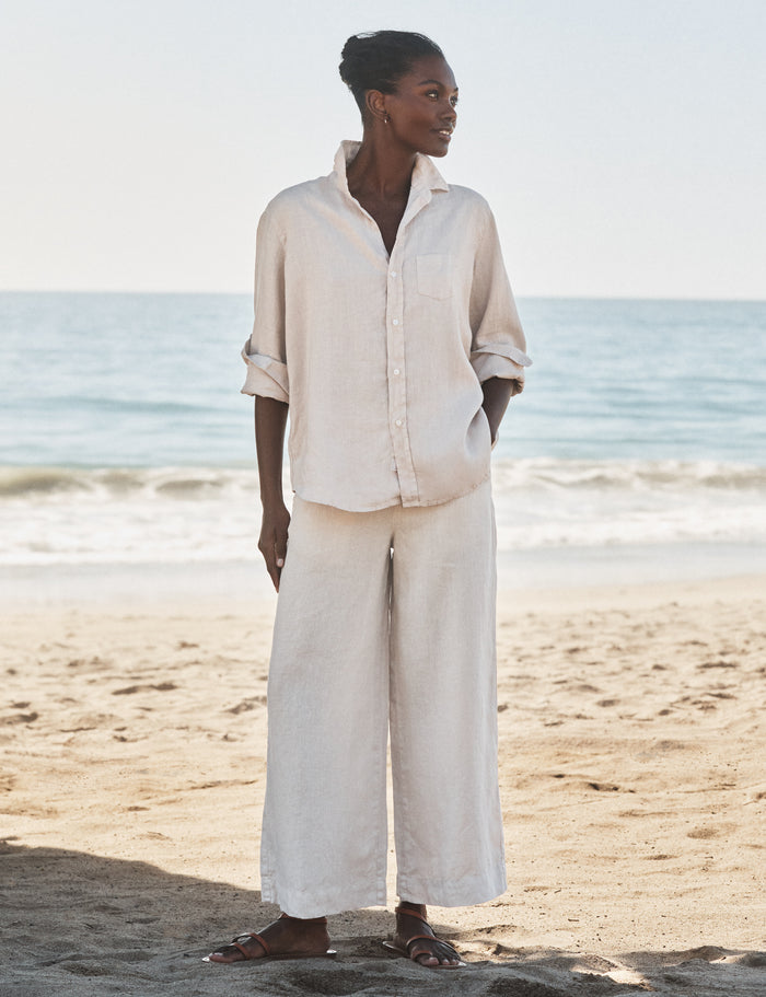Woman in beige outfit standing on a beach with ocean in the background