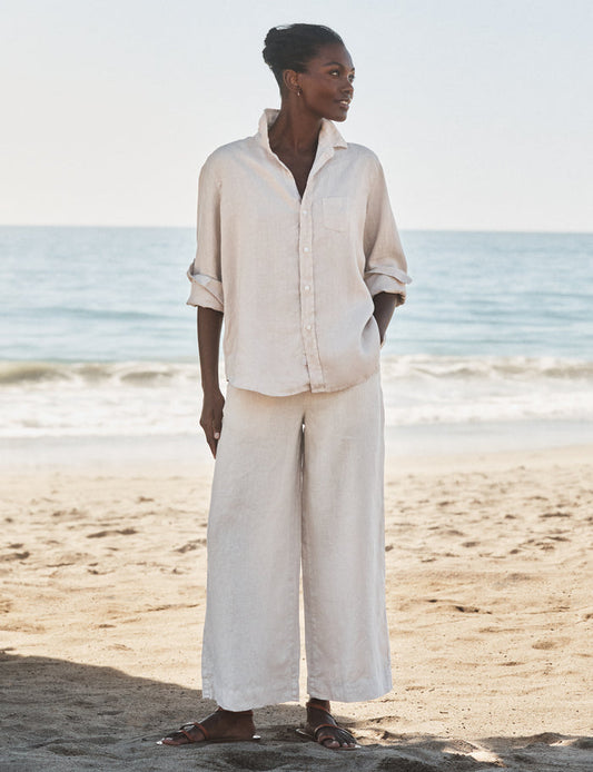 Woman in beige outfit standing on a beach with ocean in the background