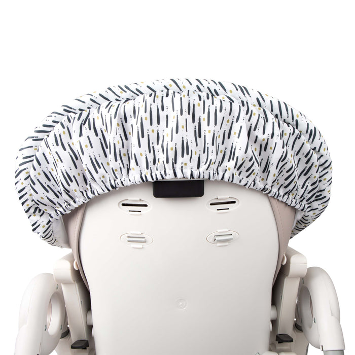 The Nuby Water-Resistant High Chair Cover, featuring black and gold brushstroke patterns, fits snugly over a white high chair. Elastic edges, multiple slots, and adjustable parts offer a secure and stylish fit.