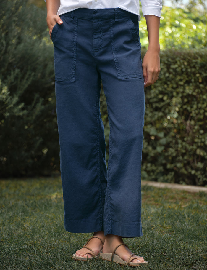 Person wearing navy blue pants standing outdoors with greenery in the background