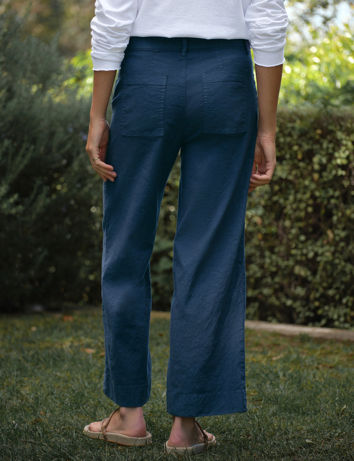 Person wearing blue pants and a white shirt standing outdoors with greenery in the background